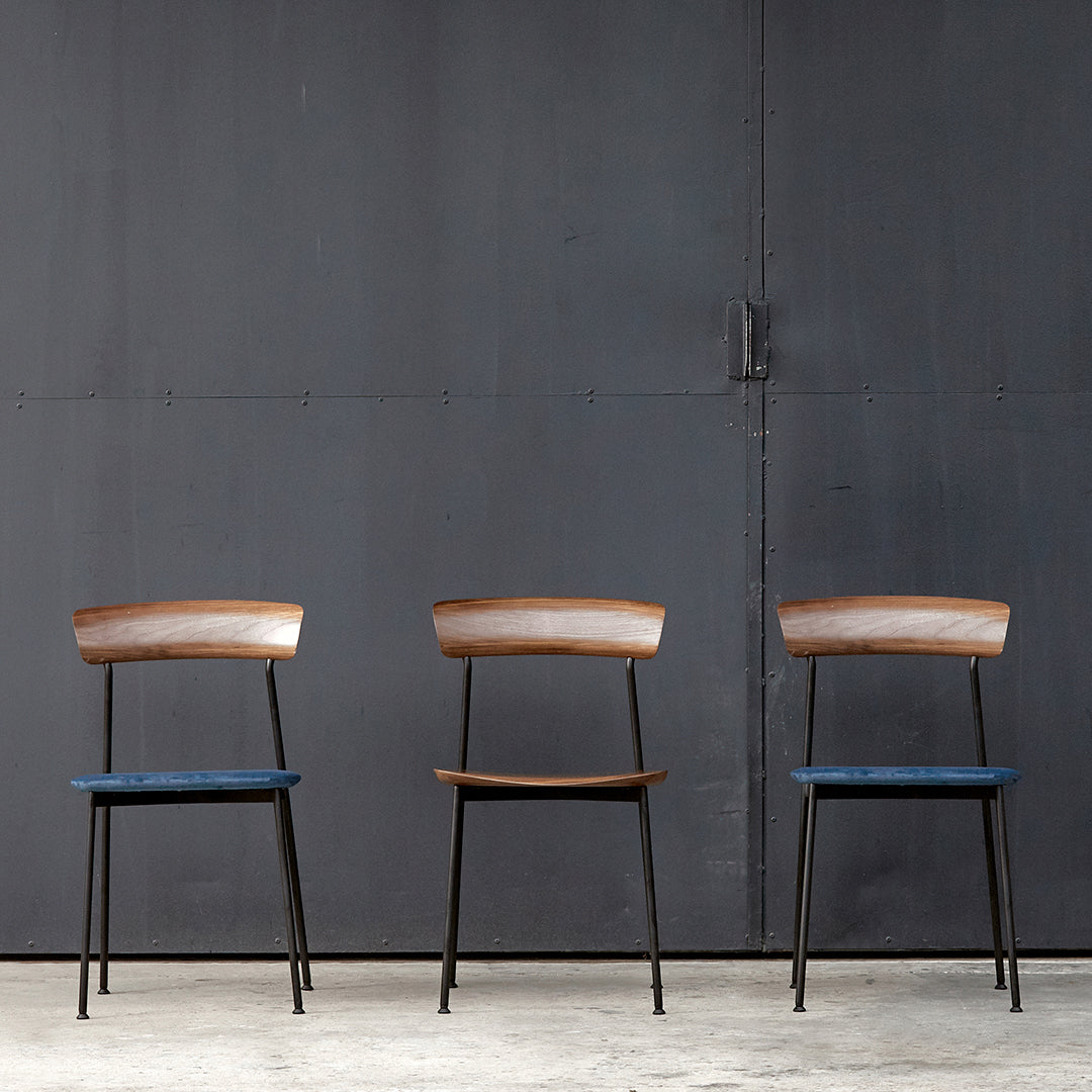 "Three modern chairs featuring brown wood and blue upholstered seats against a dark industrial backdrop."