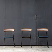 "Three modern chairs featuring brown wood and blue upholstered seats against a dark industrial backdrop."