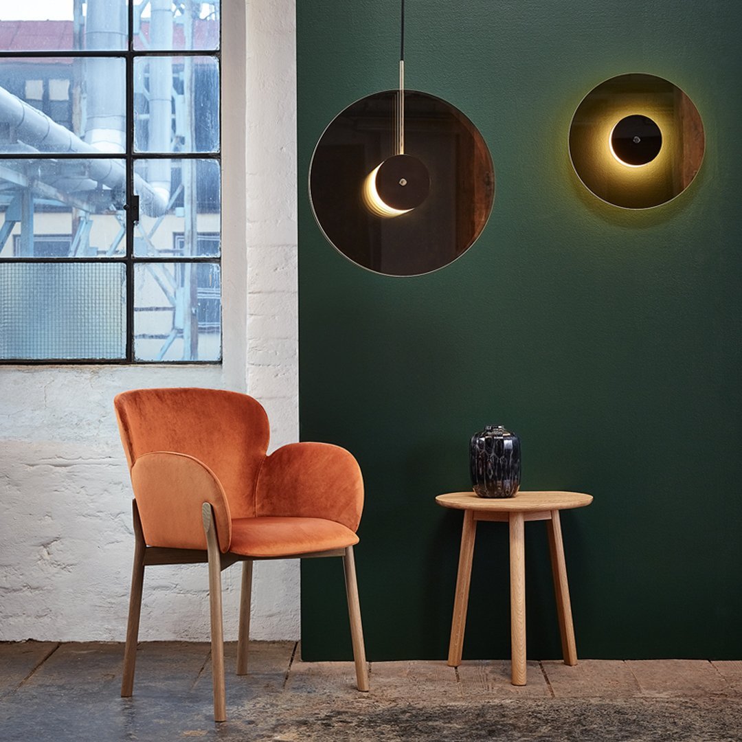 Orange velvet chair against a dark green wall, featuring circular light patterns and wooden accents.