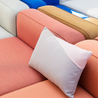 Colorful couch with coral, beige, blue, and white cushions featuring a soft pink geometric pillow design.