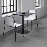 Modern black table with two minimalist white chairs on a concrete floor, featuring clean lines and neutral colors.