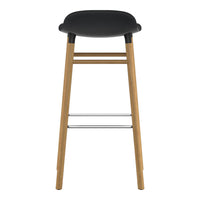 Black padded seat bar stool with natural wood legs and a chrome footrest. Modern and minimalist design.