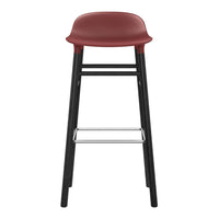 Red molded seat with sleek black legs and a chrome footrest, offering a modern, minimalist design.