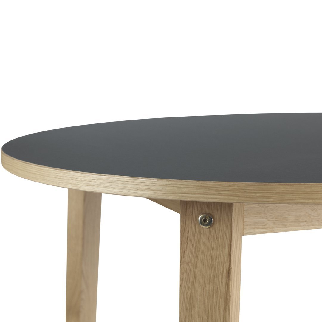 Round table with a sleek black top and light oak legs, showcasing a modern, minimalist design.