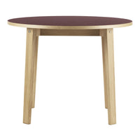 Round table with a burgundy top and natural wood legs, featuring a simple, modern design.