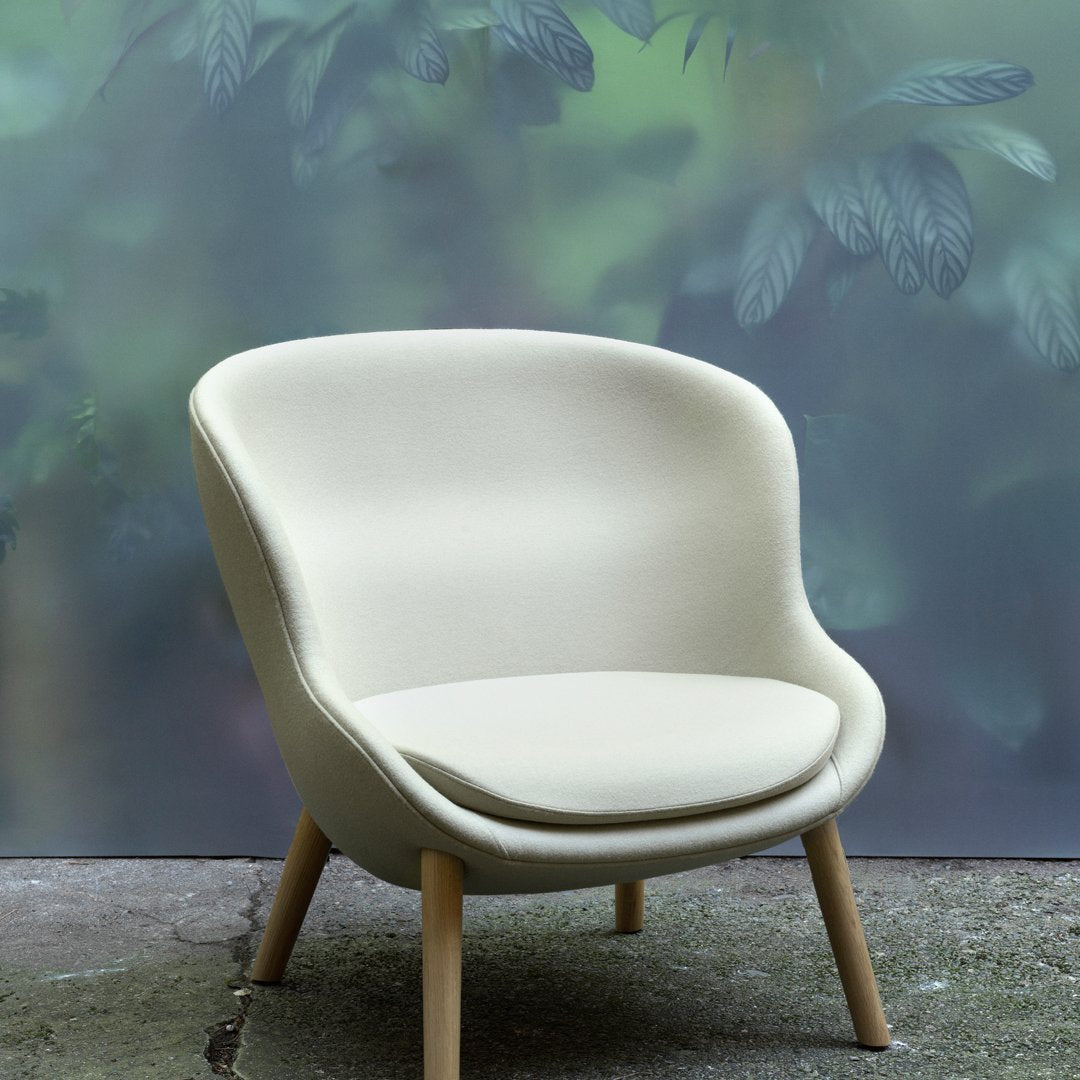 Cream-colored chair with smooth upholstery and natural wood legs, set against a soft green foliage backdrop.