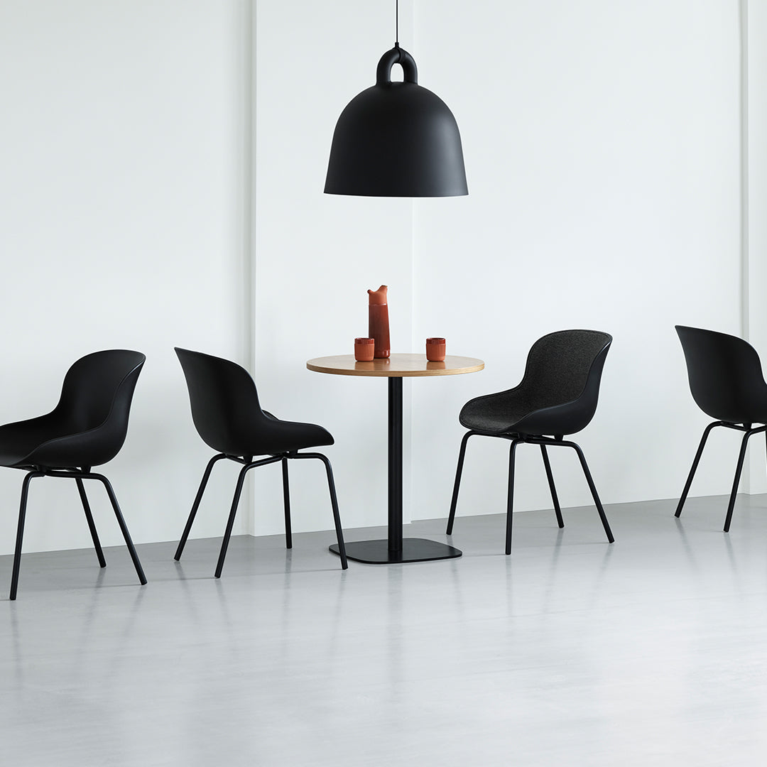 Black chairs and pendant lamp with a wooden table, set against a light gray floor and white walls. Minimalist design.