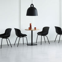 Black chairs and pendant lamp with a wooden table, set against a light gray floor and white walls. Minimalist design.