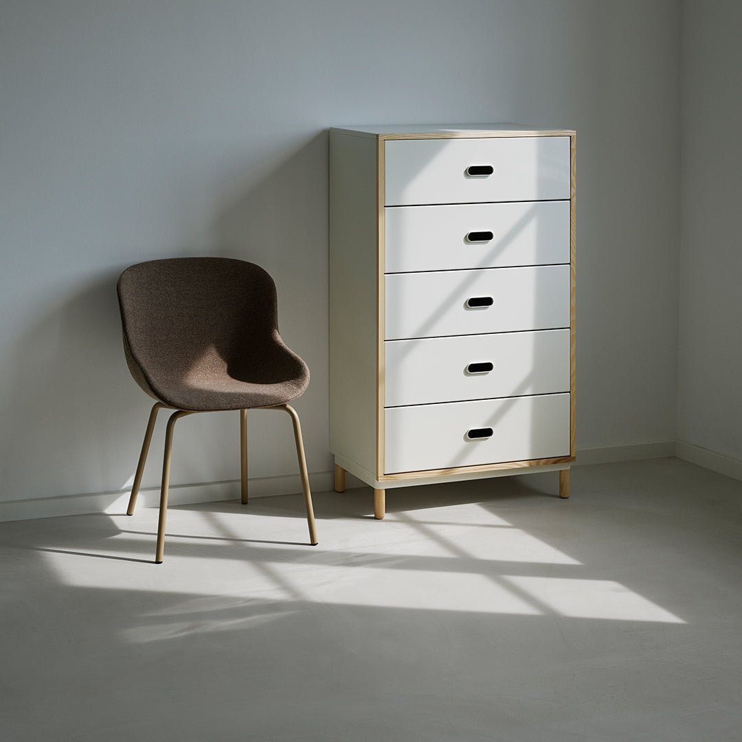 Neutral white dresser with five drawers, paired with a brown upholstered chair in a minimalist room.