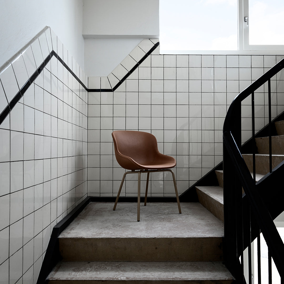 Brown leather chair on concrete stairs with black metal railing and white tiled walls. Modern minimalist design.