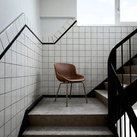 Brown leather chair on concrete stairs with black metal railing and white tiled walls. Modern minimalist design.