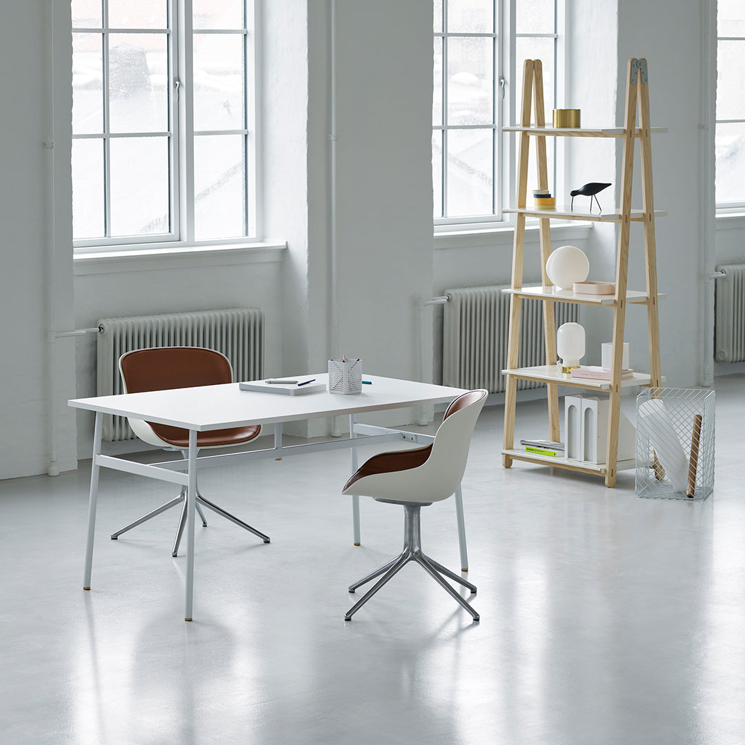 Modern white desk with sleek silver legs, paired with brown and white chairs, set in a bright, minimalistic space.