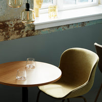 "Olive green chair with smooth upholstery next to a round wooden table, set against a rustic wall with blue and brown tones."