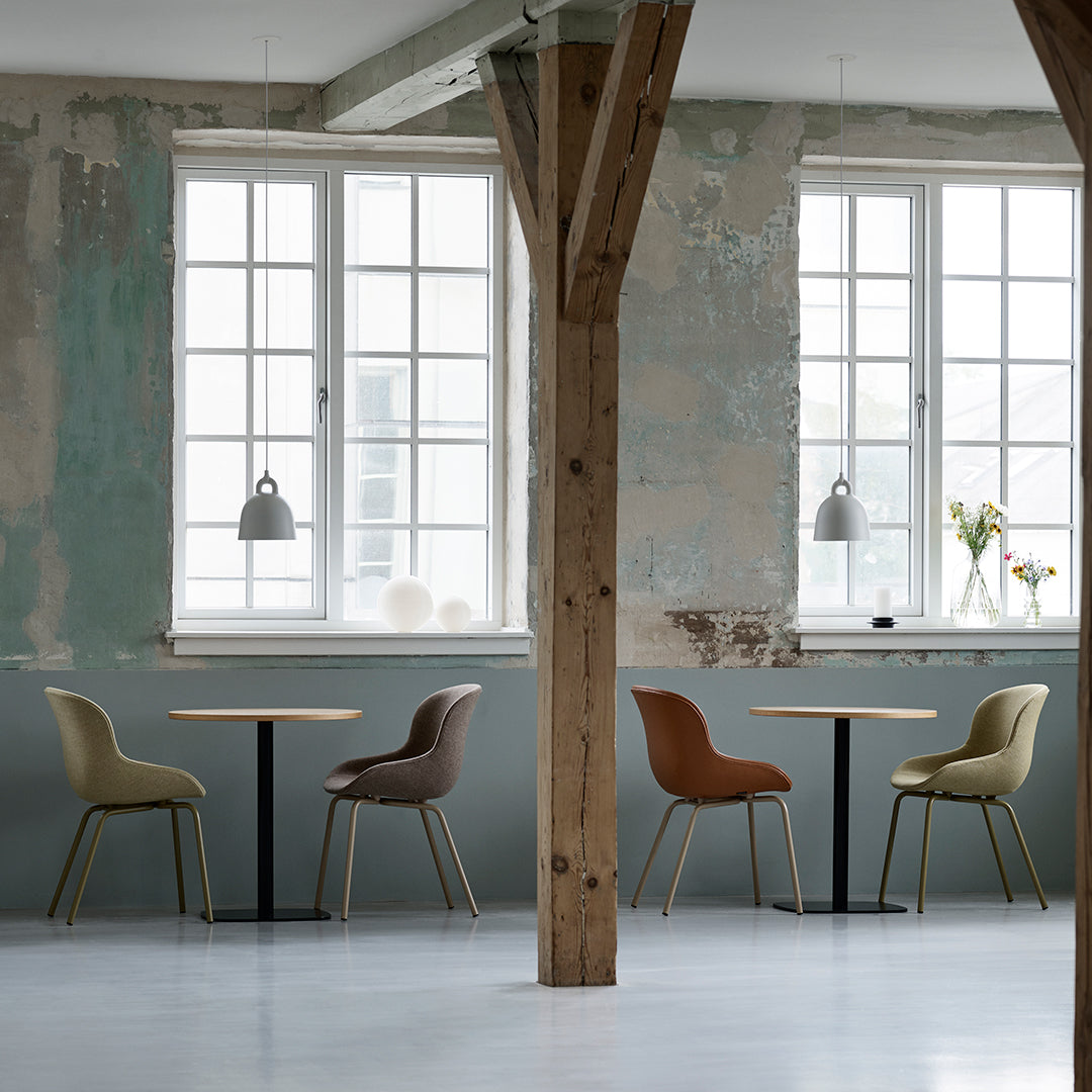 Four stylish chairs in muted green, brown, and terracotta, contrasting with a soft gray and weathered wall backdrop.