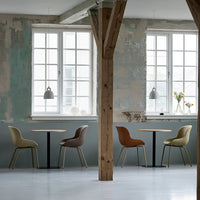 Four stylish chairs in muted green, brown, and terracotta, contrasting with a soft gray and weathered wall backdrop.