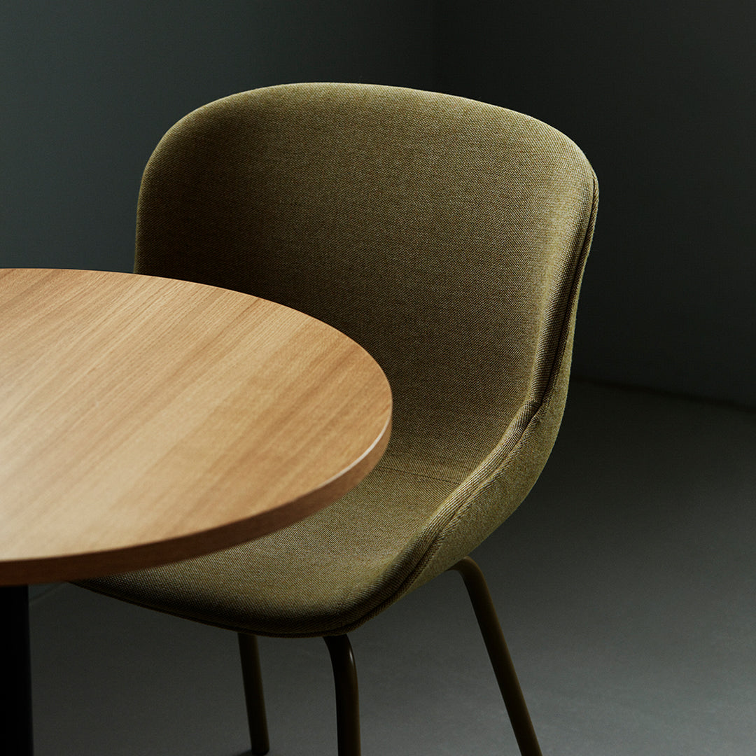 Olive green upholstered chair with a natural wood circular table on a gray background. Modern and minimalist design.