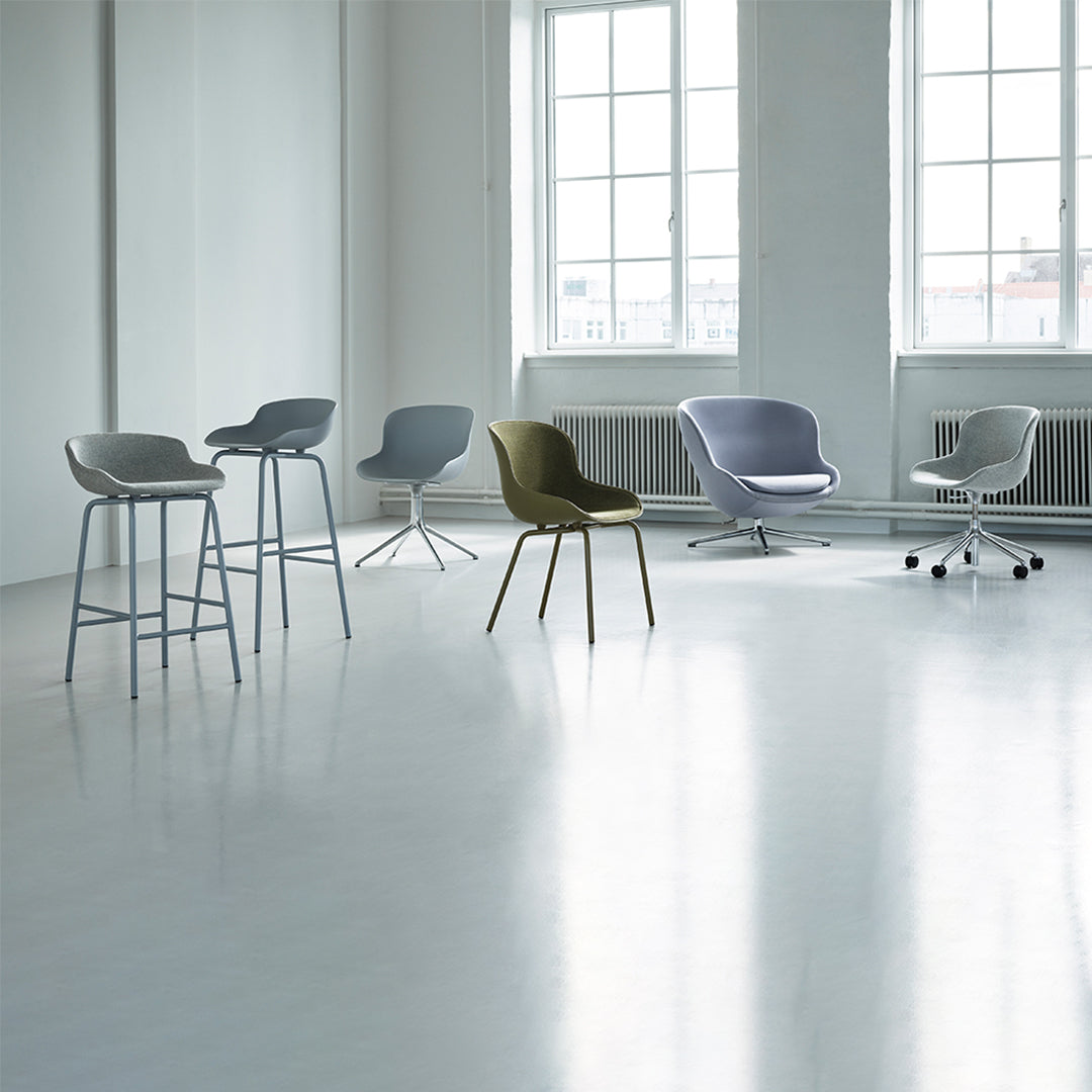 Modern chairs in soft gray, lilac, and olive hues, arranged in a bright, minimalist space with large windows.