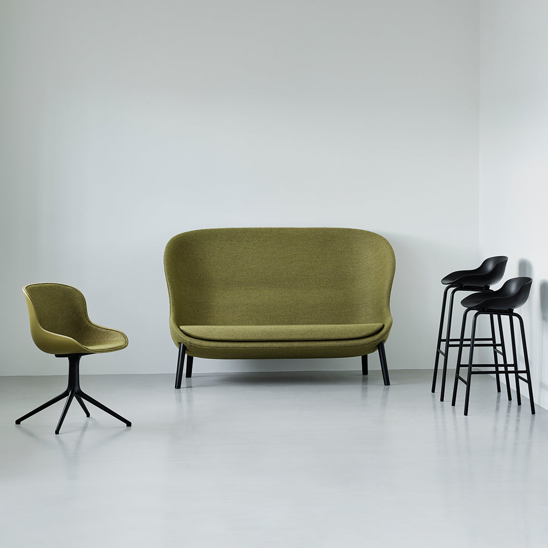 Olive green sofa and chair with smooth upholstery, complemented by sleek black bar stools. Modern minimalist design.