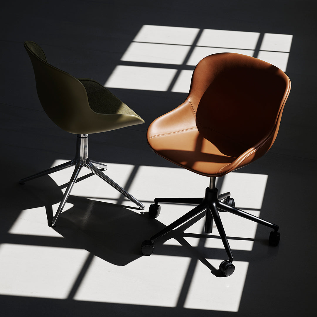 Two modern chairs, one olive green and one warm brown, set against shadows and light patterns on a floor.