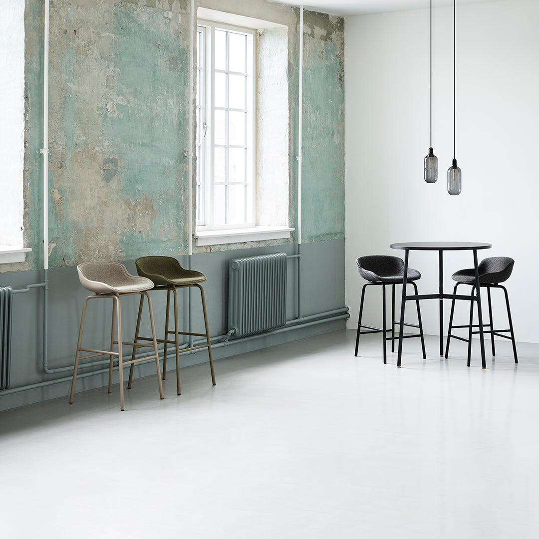Bar stools in muted tones of olive green, beige, and black, set against a textured light blue and white backdrop.