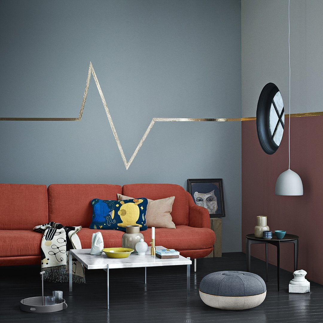 "Modern living room featuring a rust couch, geometric gold accents, and bold blue, gray, and burgundy wall patterns."