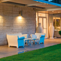 Modern white outdoor furniture set with clear glass table, complemented by a well-manicured green lawn.