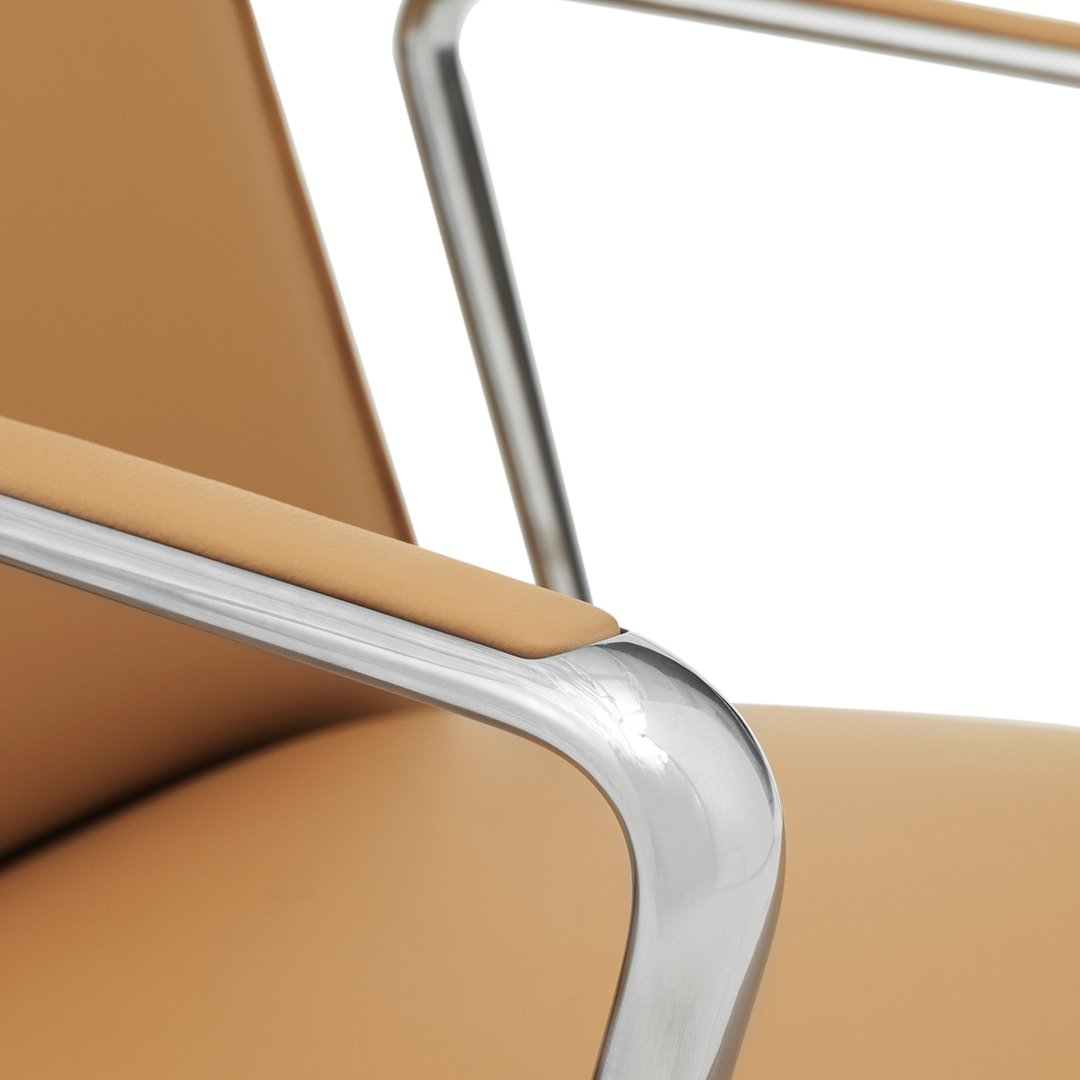 Tan leather chair with sleek silver armrests against a white background, showcasing a modern, minimalist design.