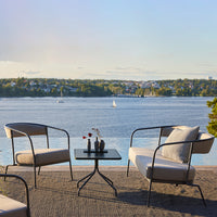 Stylish outdoor seating set in neutral tones, complemented by a black table, against a scenic waterfront backdrop.