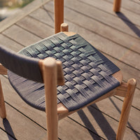 Woven black and gray chair seat with a textured pattern on a wooden patio surface.