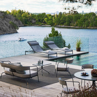 "Neutral-toned patio furniture with sleek gray cushions against a serene blue water backdrop and vibrant green scenery."