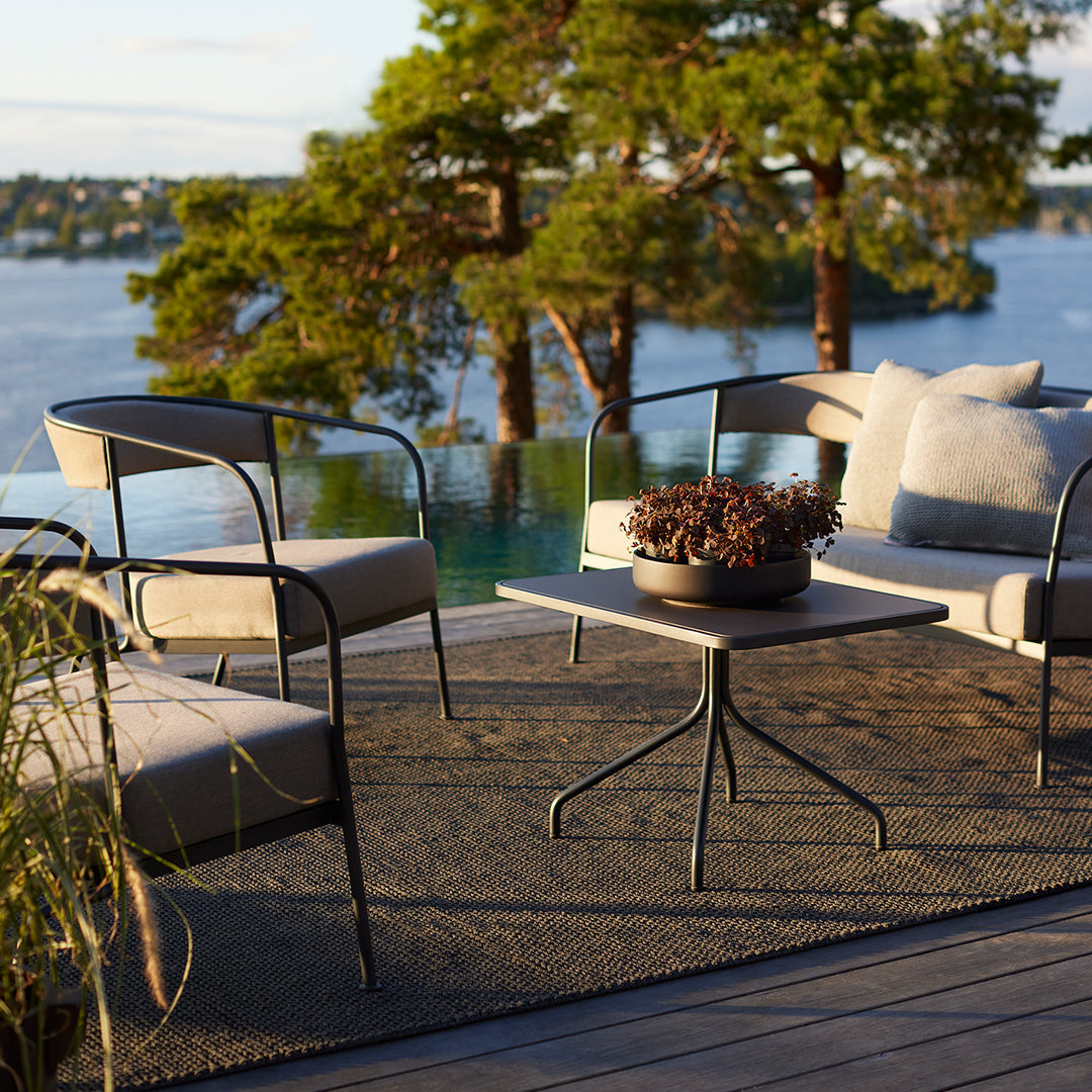 "Neutral-toned outdoor seating with black metal accents, featuring soft gray cushions and a textured, dark rug."