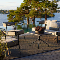 "Neutral-toned outdoor seating with black metal accents, featuring soft gray cushions and a textured, dark rug."