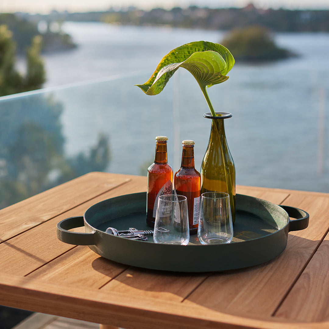Green round tray with textured dark green, surrounded by amber bottles and clear glasses on a wooden table.