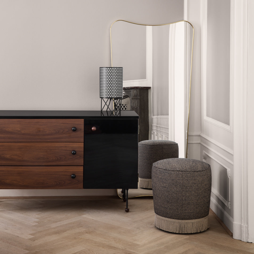 Stylish wood and black cabinet with gray patterned stool, soft beige tones, and elegant gold floor lamp.