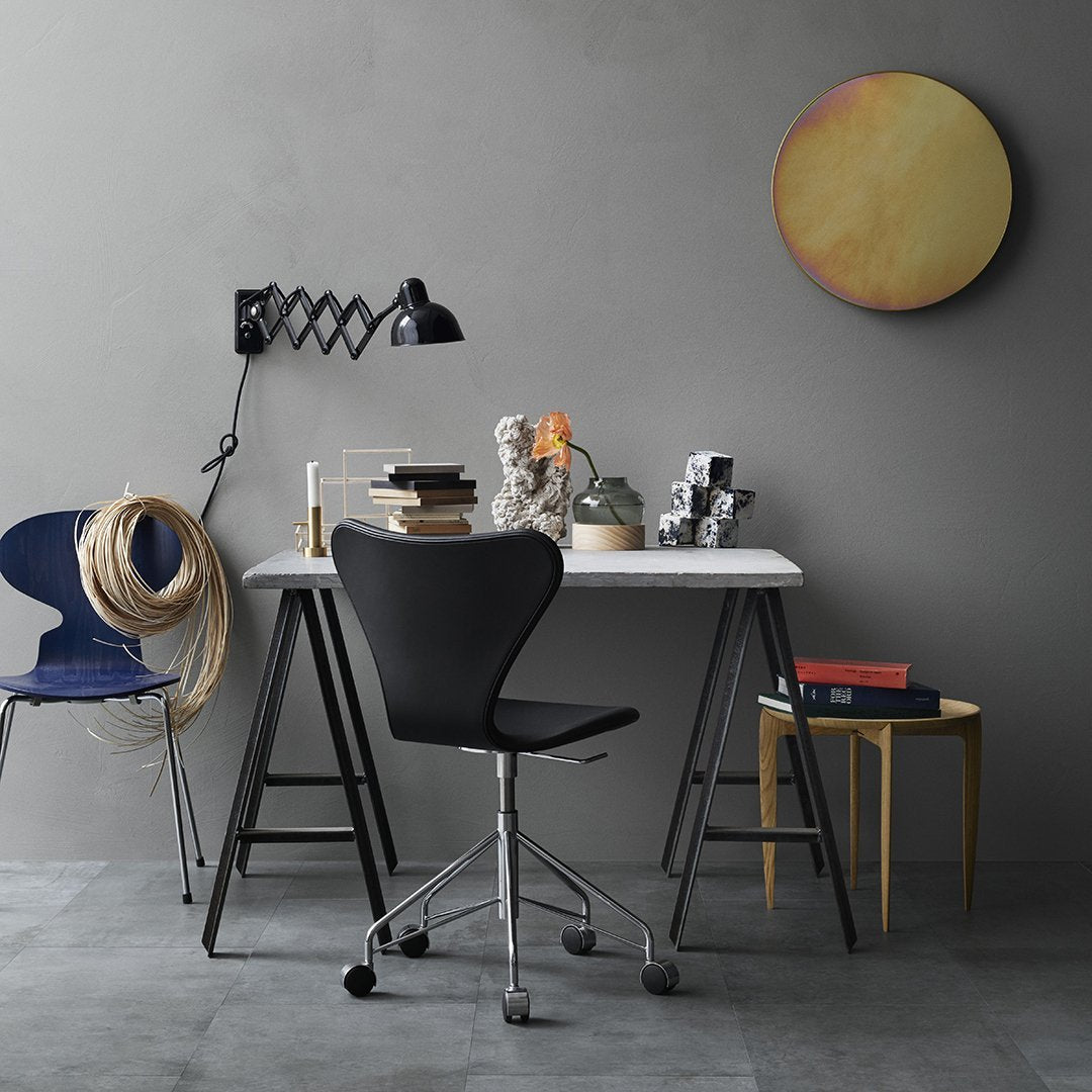 Modern desk setup featuring a black chair, blue accent chair, gray walls, and a round yellow wall art piece.