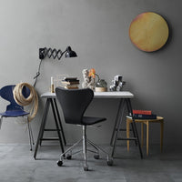Modern desk setup featuring a black chair, blue accent chair, gray walls, and a round yellow wall art piece.