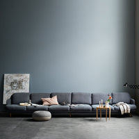 Modern gray sofa with sleek lines and light pink cushions, set against a soft blue wall and minimalist decor.