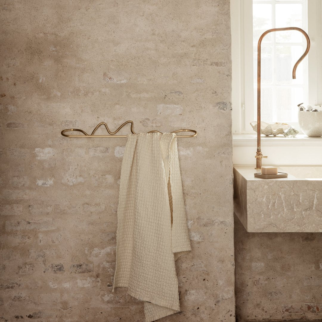 Beige textured towels hanging on a brass rack against a rustic stone wall, creating a warm and cozy aesthetic.