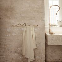 Beige textured towels hanging on a brass rack against a rustic stone wall, creating a warm and cozy aesthetic.