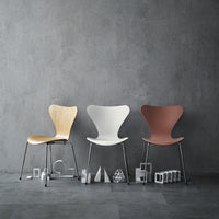 Three stylish chairs in natural wood, white, and rust red, set against a textured gray backdrop. Modern design and clean lines.