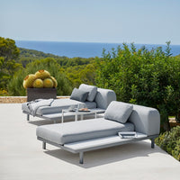 Modern gray lounge chairs with sleek lines and minimalistic design, set against a lush green landscape and blue ocean view.