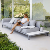 Grey outdoor sofa with minimalist design, featuring soft cushions and a sleek white side table in a serene setting.