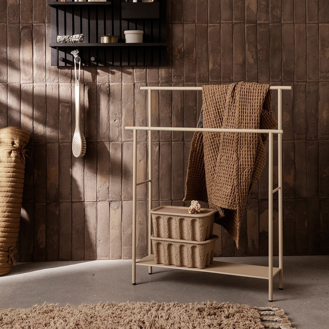 Beige metal rack with textured woven blanket and baskets, set against wood-patterned wall and earthy tones.