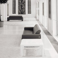 "Modern black sofa and white table set against a minimalist, light-filled space with textured wall art."