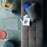 Gray and blue patterned pillows on a soft brown ottoman, surrounded by neutral tones and modern decor elements.