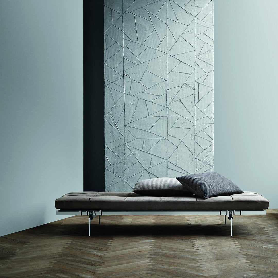 Minimalist sofa in soft taupe, with grey geometric wall pattern and light wood herringbone floor. Modern decor accents visible.