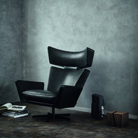Stylish black armchair with sleek lines against a textured gray wall and warm-toned floor.