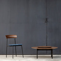 Mid-century modern chair with a dark wood back and blue seat, paired with a round wooden coffee table on a gray backdrop.