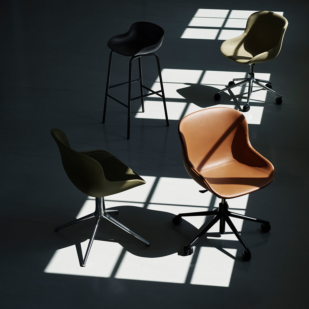Four stylish chairs in olive green, black, warm brown, and cream, with sleek modern designs casting shadows.