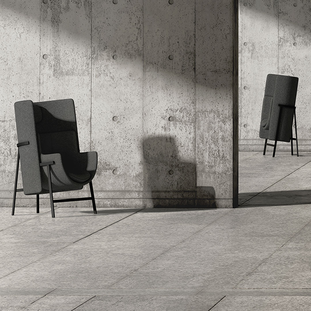 "Gray upholstered chair with a minimalist design set against a textured concrete backdrop."